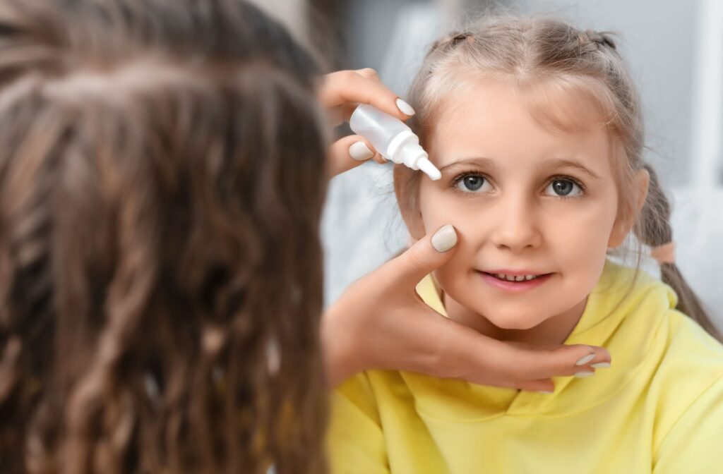 A woman helps her young daughter by placing atropine eye drops in her eyes to slow myopia progression