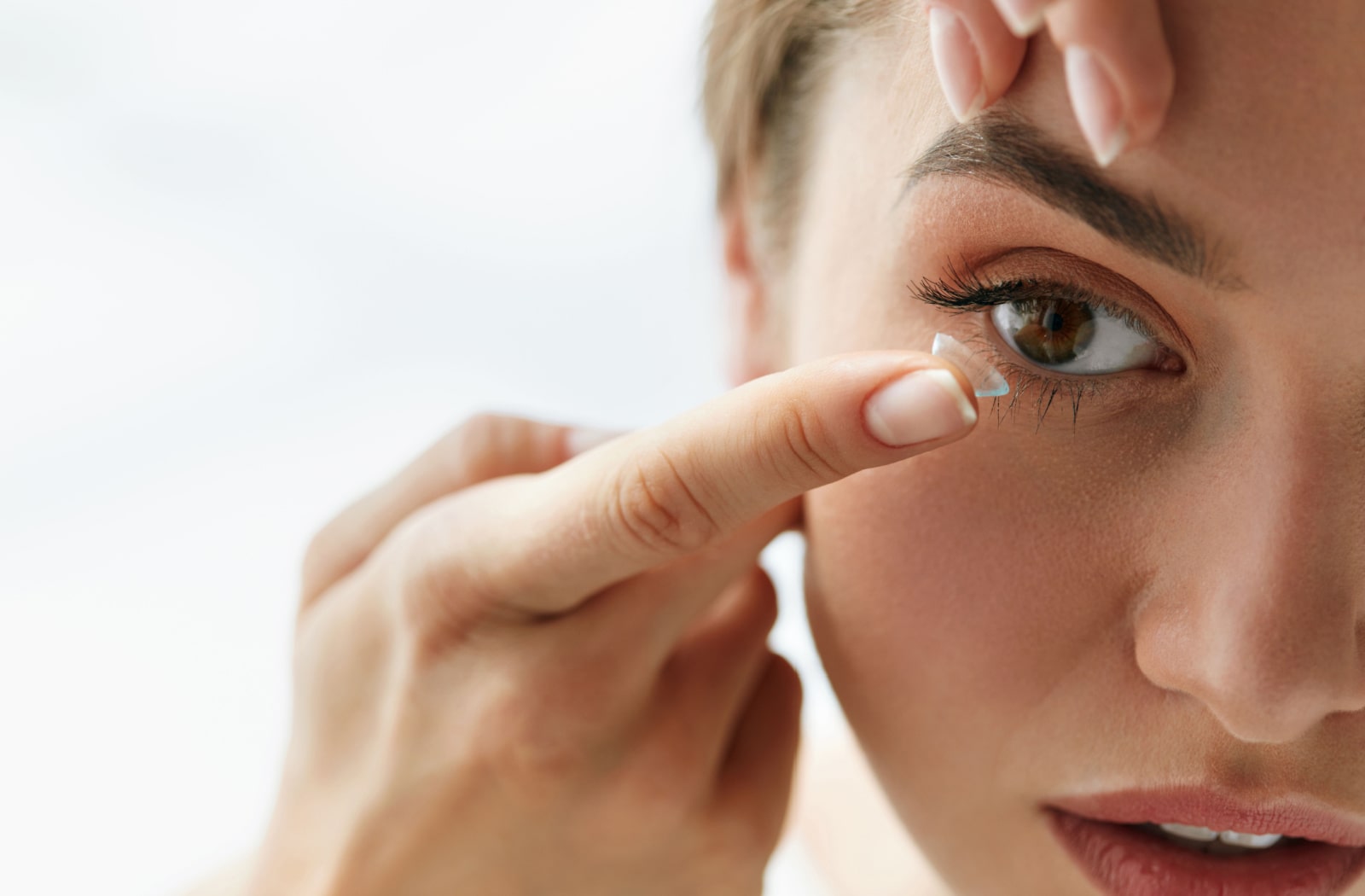 A close up image of a woman placing a contact lens into her right eye