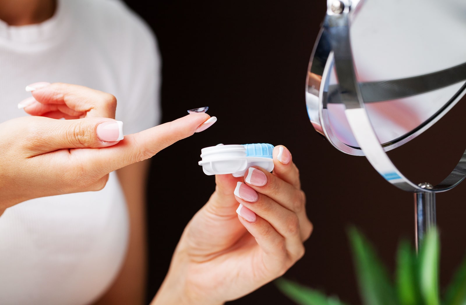 A woman removing a contact lens from her eye and placing it back into a contact lens case.