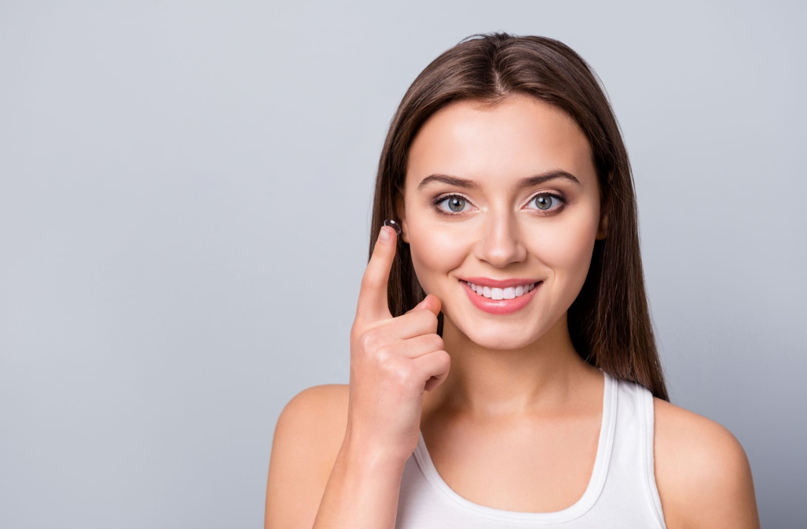 A woman smiling and holding onto a contact lens on her right index finger