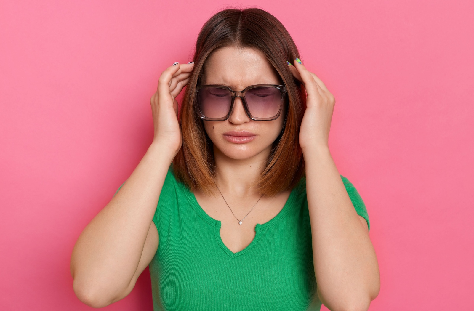 A person wearing sunglasses clutches their head due to dizziness.