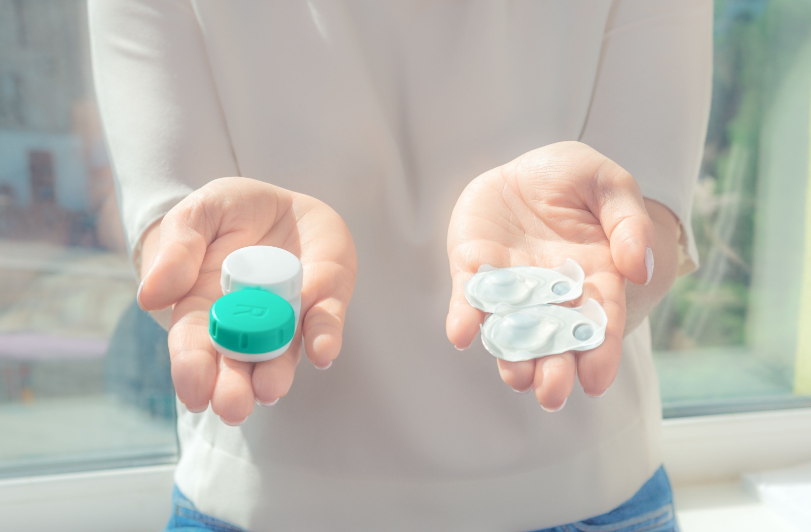 An individual holds out a pair of contact lenses in each hand, just two of the many options available for those with dry eye.