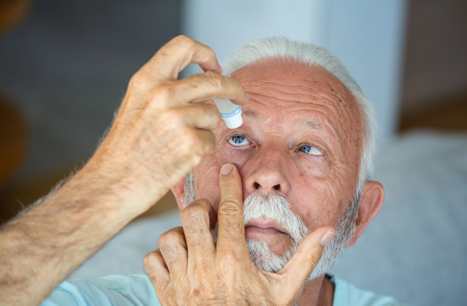 An older person putting eye drops into his eye.