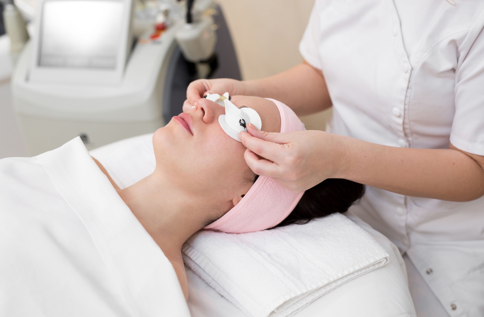 A person lies on a treatment bed while a eye doctor places protective goggles over their eyes.